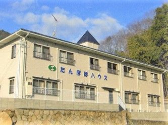 たんぽぽハウスの看板が壁に掲げられている施設の外観。洋風の三角屋根が付いている２階建ての建物