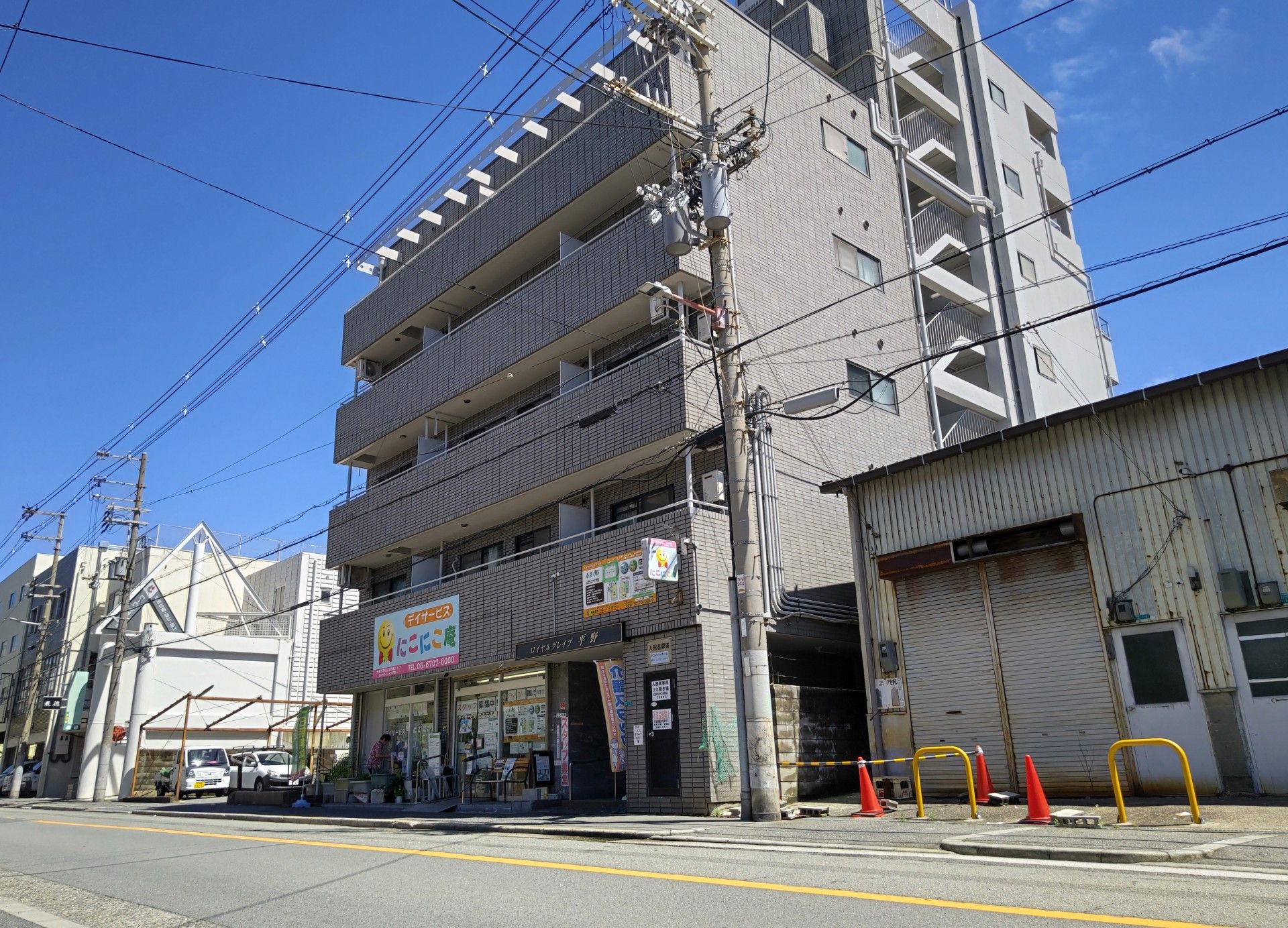 ５階建て部分と７階建て部分が繋がった形のビルで、大通りに面している。施設横の土地には車が停まっている。