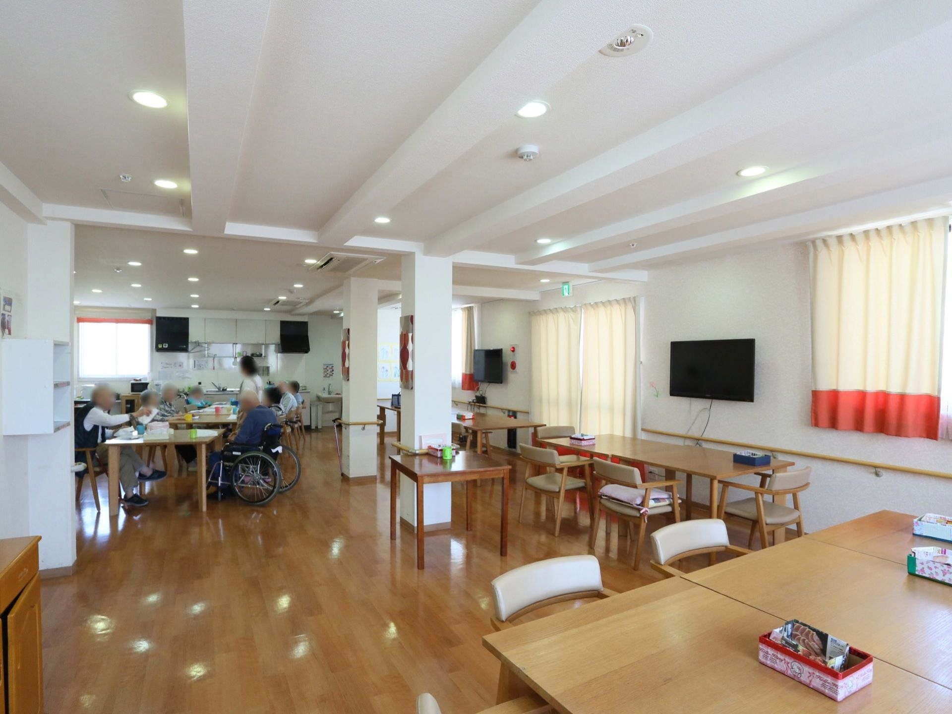 白い天井と壁が開放感を与えている食堂である。壁には大型液晶テレビが２台備わっている。手すりがあるので安全に歩行ができる。