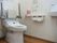 明るく清潔感のある共有トイレである。背もたれのクッションや折り畳み式の手すり、ナースコールが完備されている。