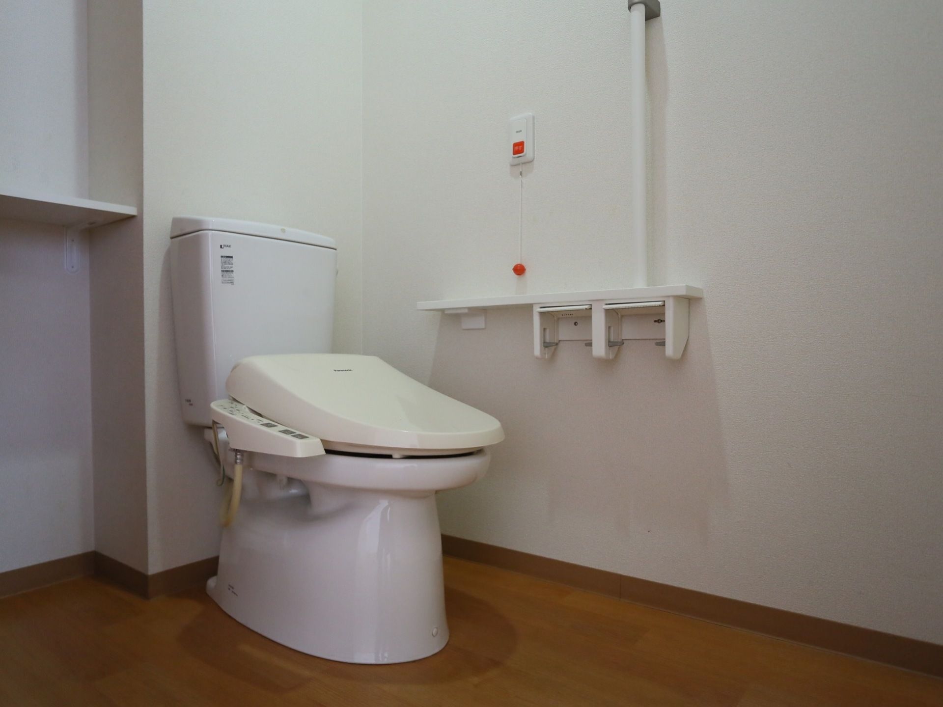 温水洗浄便座が付いているトイレがある。壁には手すりがあり、ペーパーホルダーが２つある。物を置く棚が設置されている。