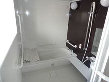 手すりがたくさん設置された一人用の浴室にはオレンジの呼び出しボタンやシャワーもあり、浴槽にはふたが置かれている。