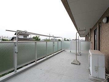 洗濯物干しが元々取り付けられているバルコニーには、移動式の物干しざおもあり、周辺には民家がある。