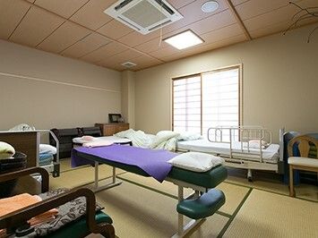 障子が設置された大きな窓が付いたそばにはベッドが置かれ、いすなどの家具も置かれている。