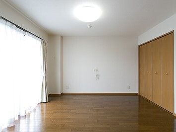 レースカーテンとカーテンが付いた大きな窓があり、ベッドサイドには緊急通報装置があり、大きな収納スペースもある。