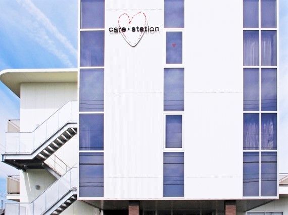 白い建物の外壁にはハートのイラストと住宅名が書かれ、屋外階段やベランダもある。