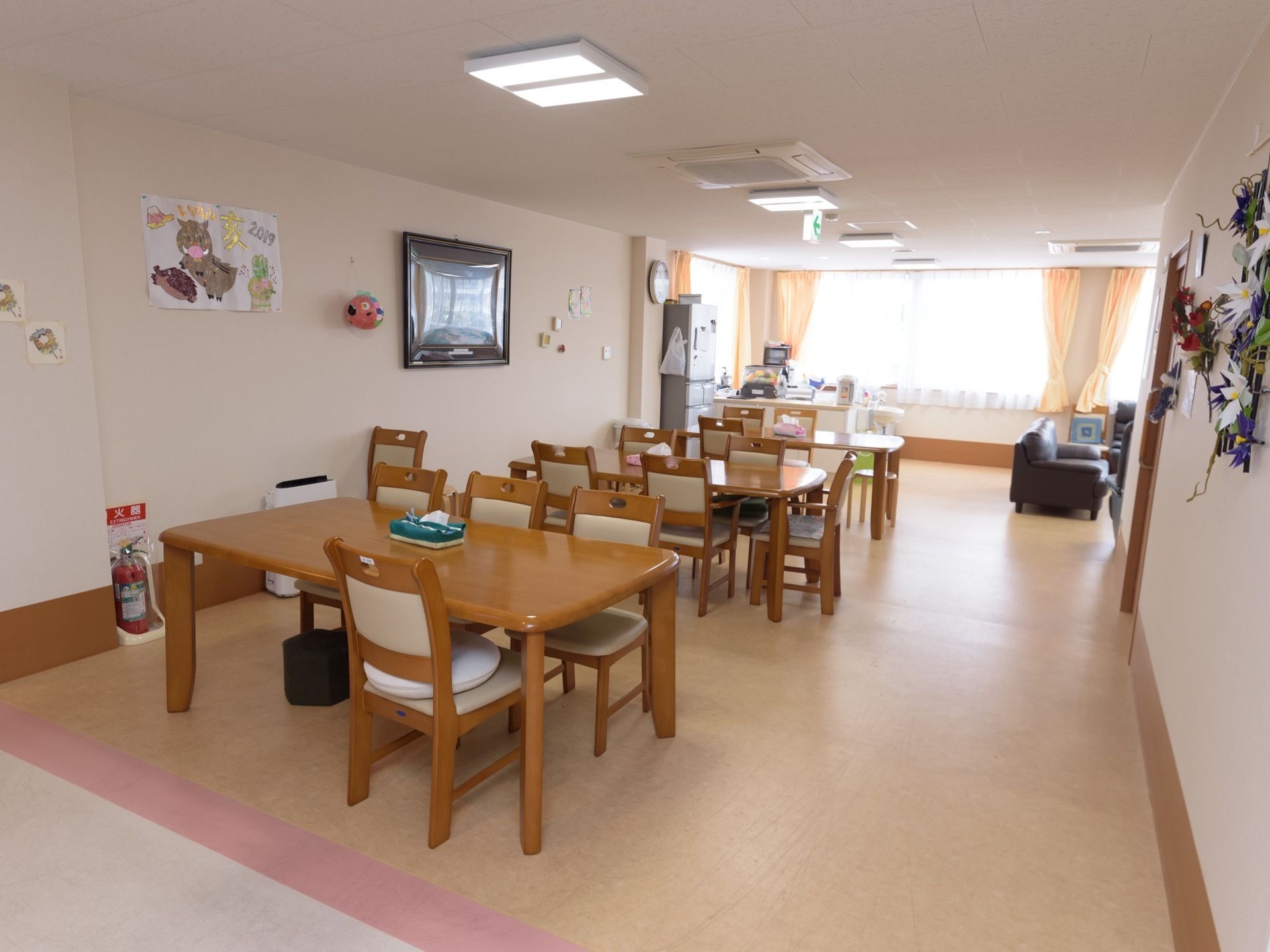廊下と仕切りのない食堂で、壁にはテレビがある。奥にキッチンスペースがあり、冷蔵庫が置かれている。