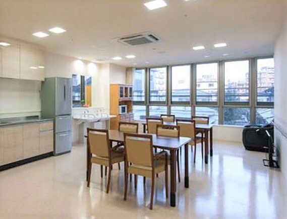 冷蔵庫やキッチンが設置され、奥の食器棚には電子レンジもある。4人掛けのテーブルセットが二つ置かれ、大きな窓が付いている。