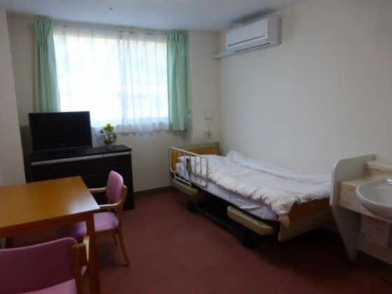 カルテを見ながら話しているエプロンを付けた女性スタッフ。カーディガンを着た高齢女性が聞いている。
