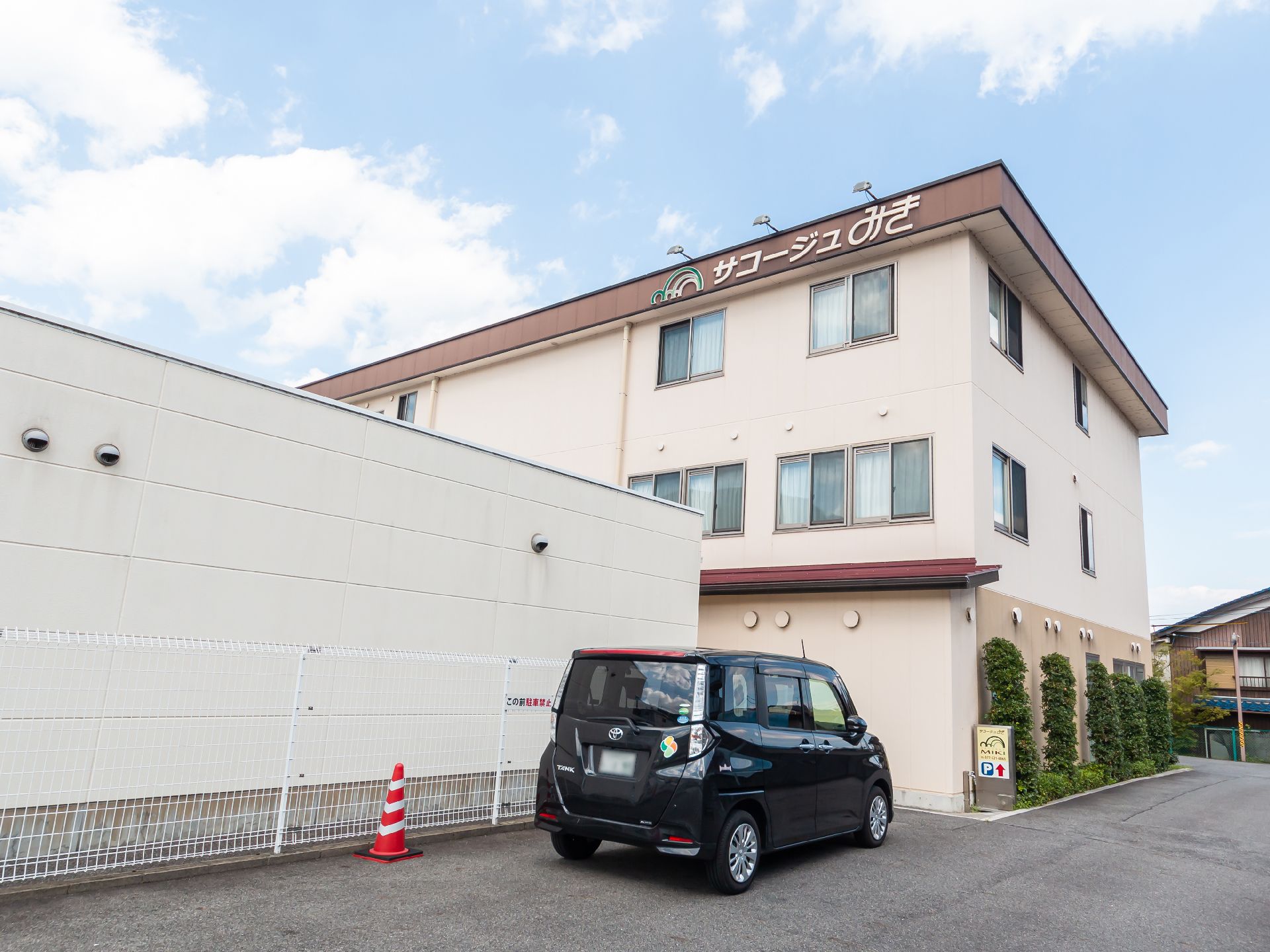 アスファルトに隣接したベージュの外観で３階建ての建物