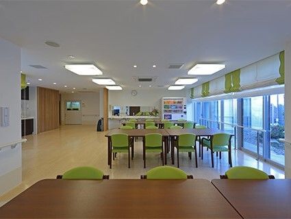 厨房が奥に貼り、フローリングのスペースにはライトグリーンの椅子がセットされた木製のテーブルが複数置かれている。