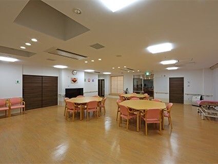 ピンクの椅子がセットされた木製のテーブルが複数置かれ、テレビもあるゆったりとした共有スペース。