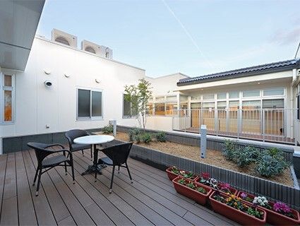 花が植えられたプランターが複数置かれたウッドデッキのテラス。ガーデン用のテーブルセットがある。