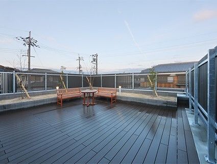 花壇が設置されたウッドデッキのテラス。木製のベンチや円形のテーブルが置かれている。