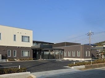 白とダークグレーの外壁の建物は2階建てで敷地内には駐車場があり、玄関に屋根がある。