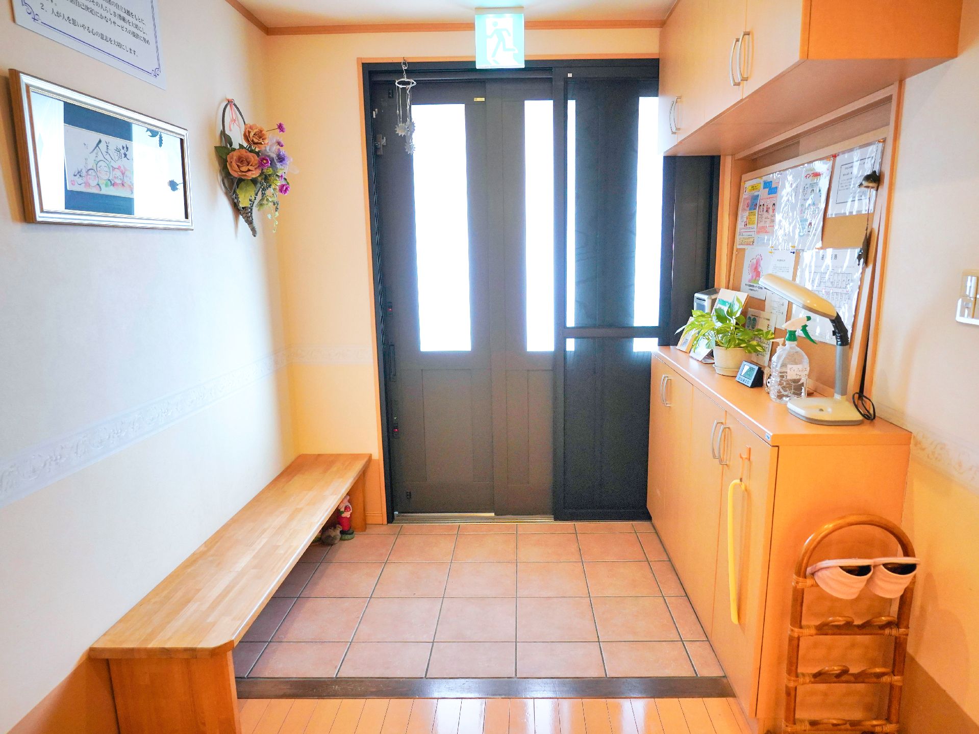 エプロンを付けた女性スタッフとニット帽をかぶった車いすの高齢女性が屋外で笑顔で過ごしている。