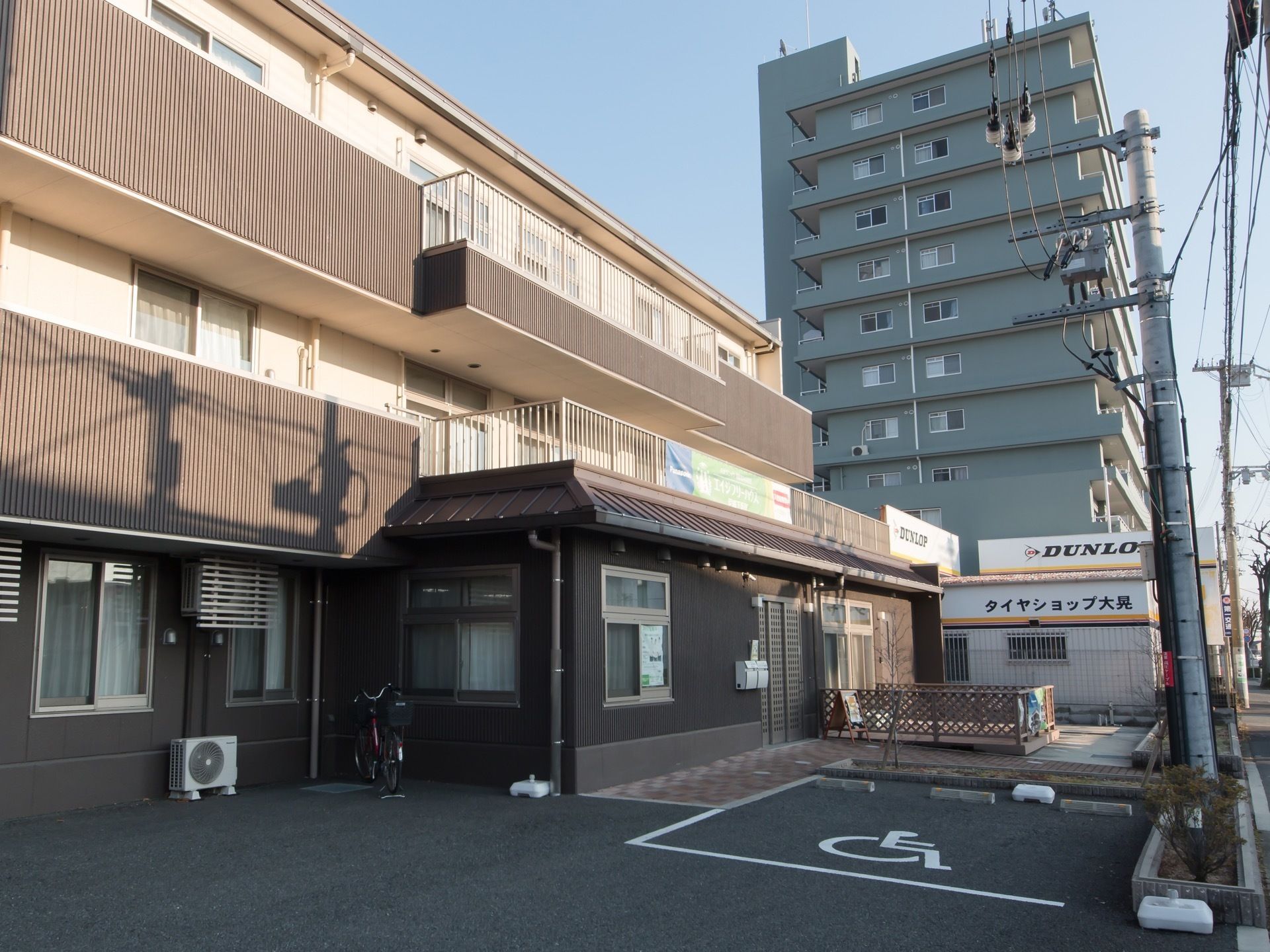 住宅街の中にある住まいで、敷地内にアスファルトで舗装された駐車場が設けられている。建物沿いに、自転車が１台置かれている。