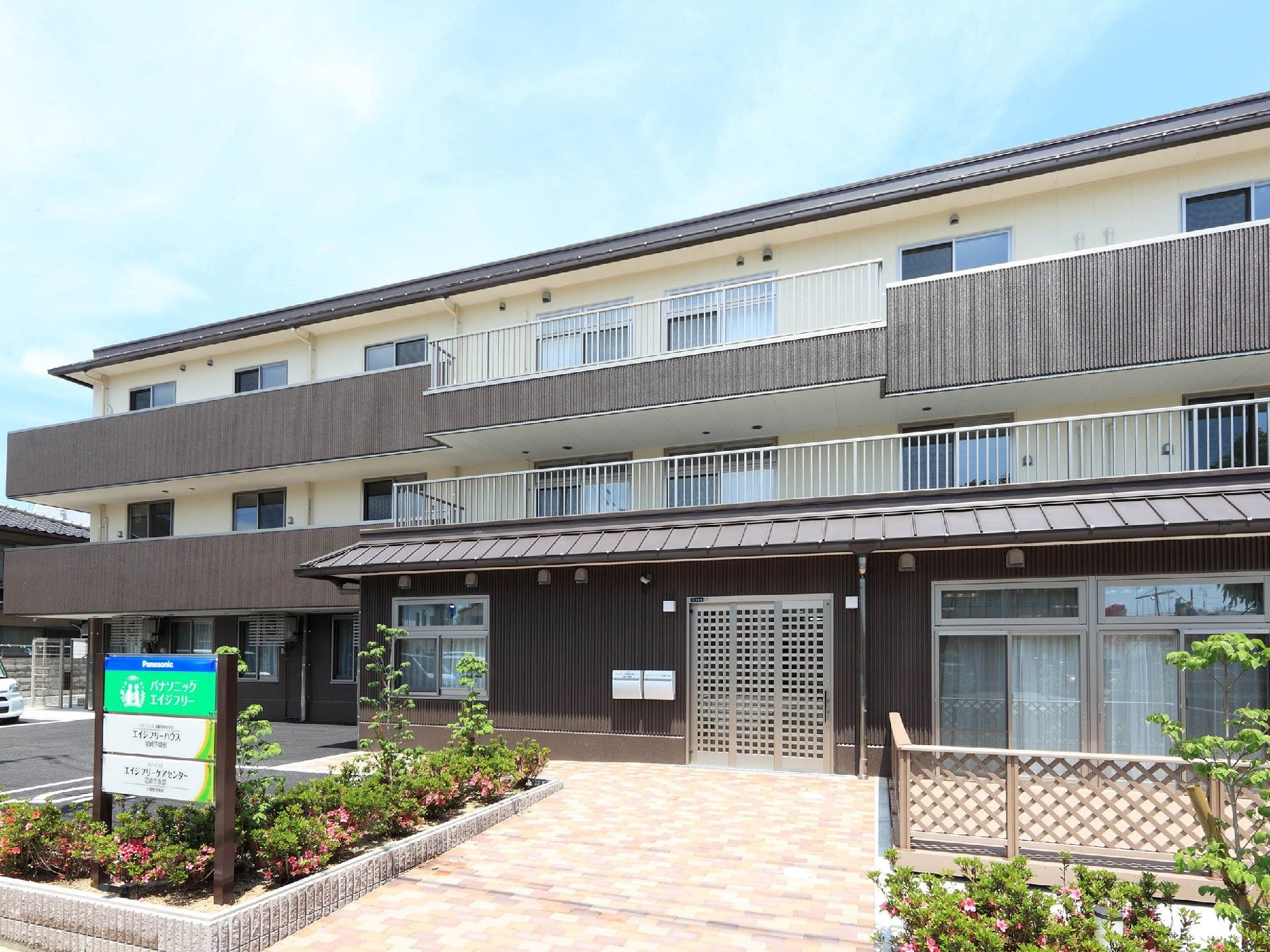 3階建ての建物にはベランダが付き、玄関の周りには木や花も植えられ、ウッドデッキや駐車スペースも設置されている。