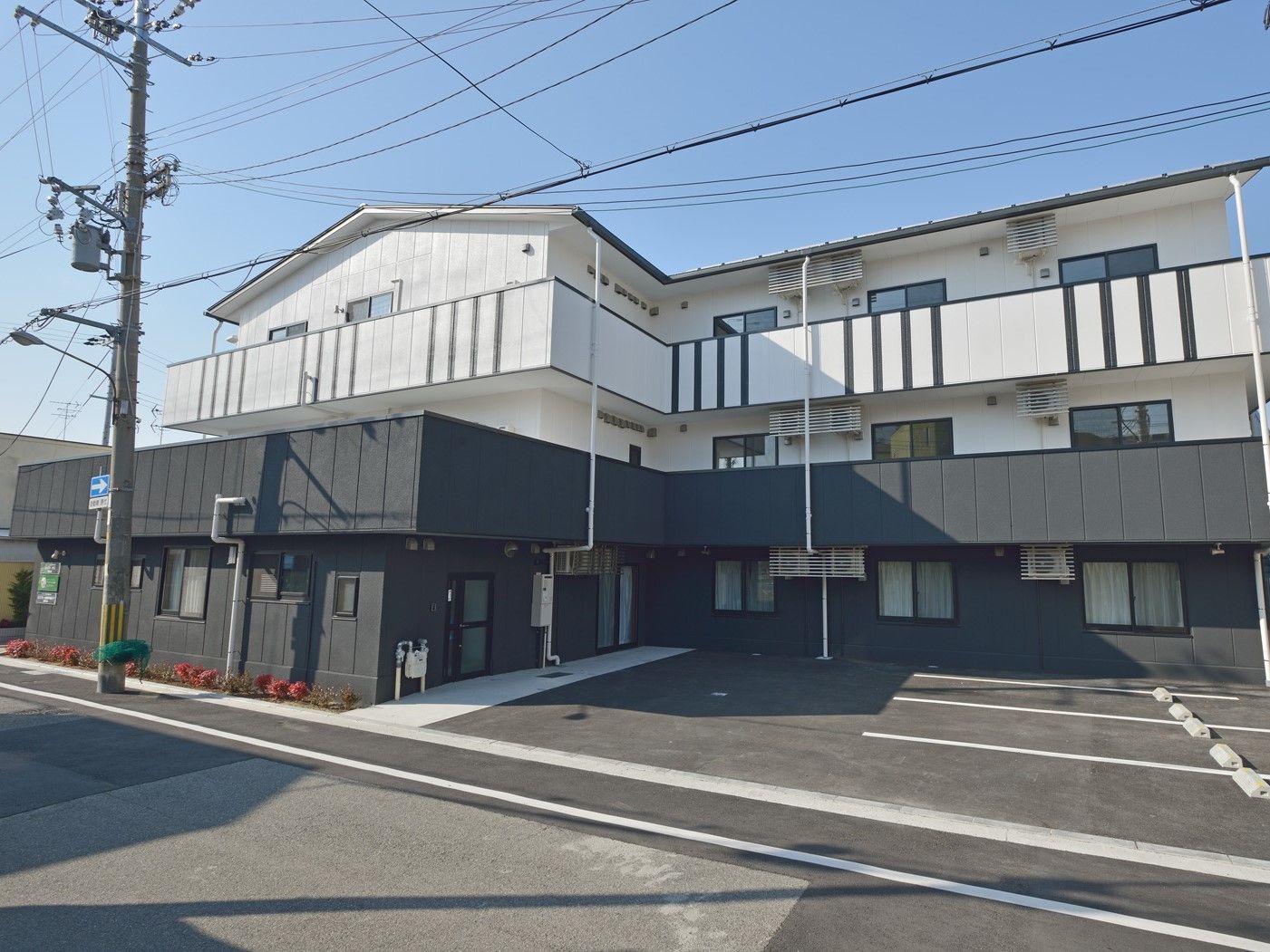 白とダークグレーの3階建ての建物にはベランダや駐車場も付いている。