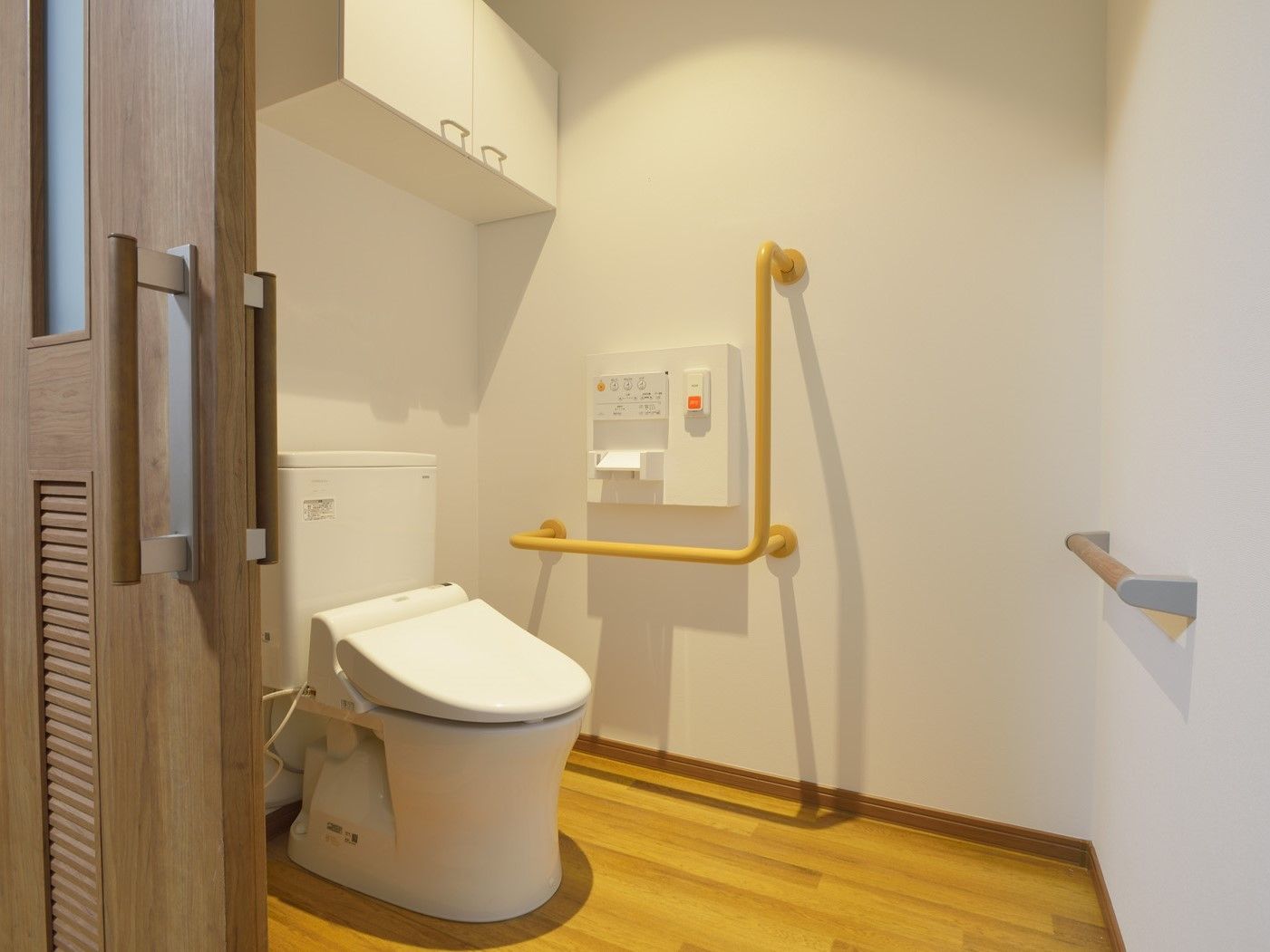 引き戸が付いたトイレは広く、壁にはエル字型の手すりや呼び出しボタンが付いている。