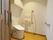 エル字型の手すりが設置されたトイレには、壁に操作パネルが付き、オレンジの呼び出しボタンや大きめの収納棚もある。