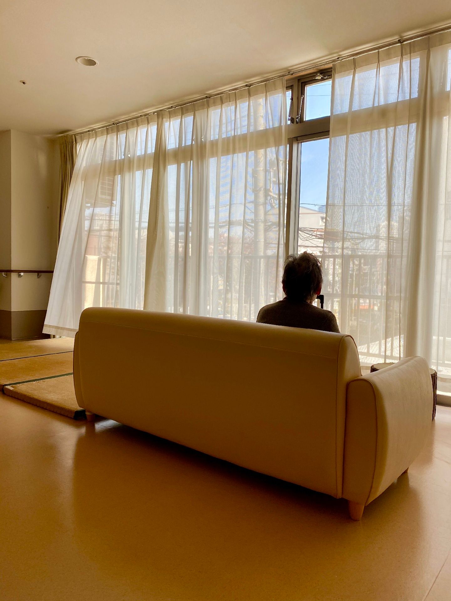 黄色みのあるソファに人が座って目前の窓の向こうの景色を眺めている。