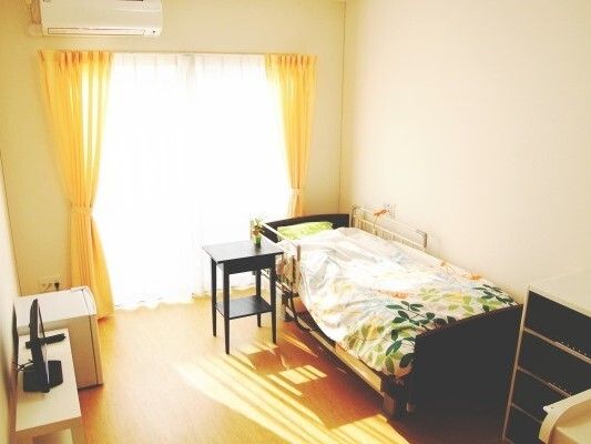陽の光の差す部屋。介護ベッドや棚、テレビ、冷蔵庫、エアコン等が置いてある
