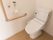 トイレに洗浄暖房機能つきの便座が設置されている。壁にL字型の大きな手すりが付けられているオレンジ色の呼び出しボタンがある。