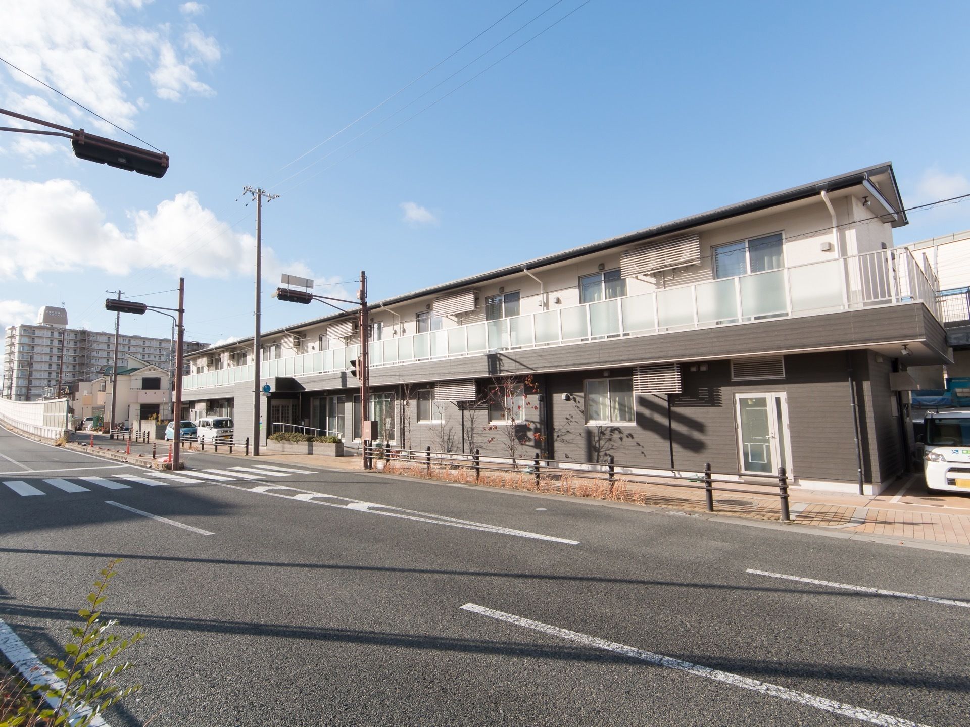日当たりのよい敷地に建っている２階建ての施設である。施設の前に広い歩道があり、信号がついた横断歩道もある。