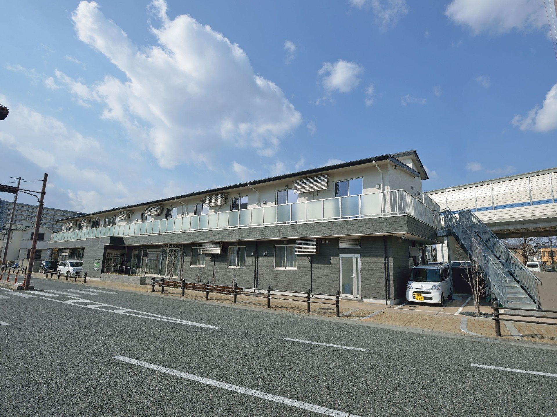 横に長い長方形の建物は2階建てで、1階の一部分がダークグレー。駐車スペースもある。
