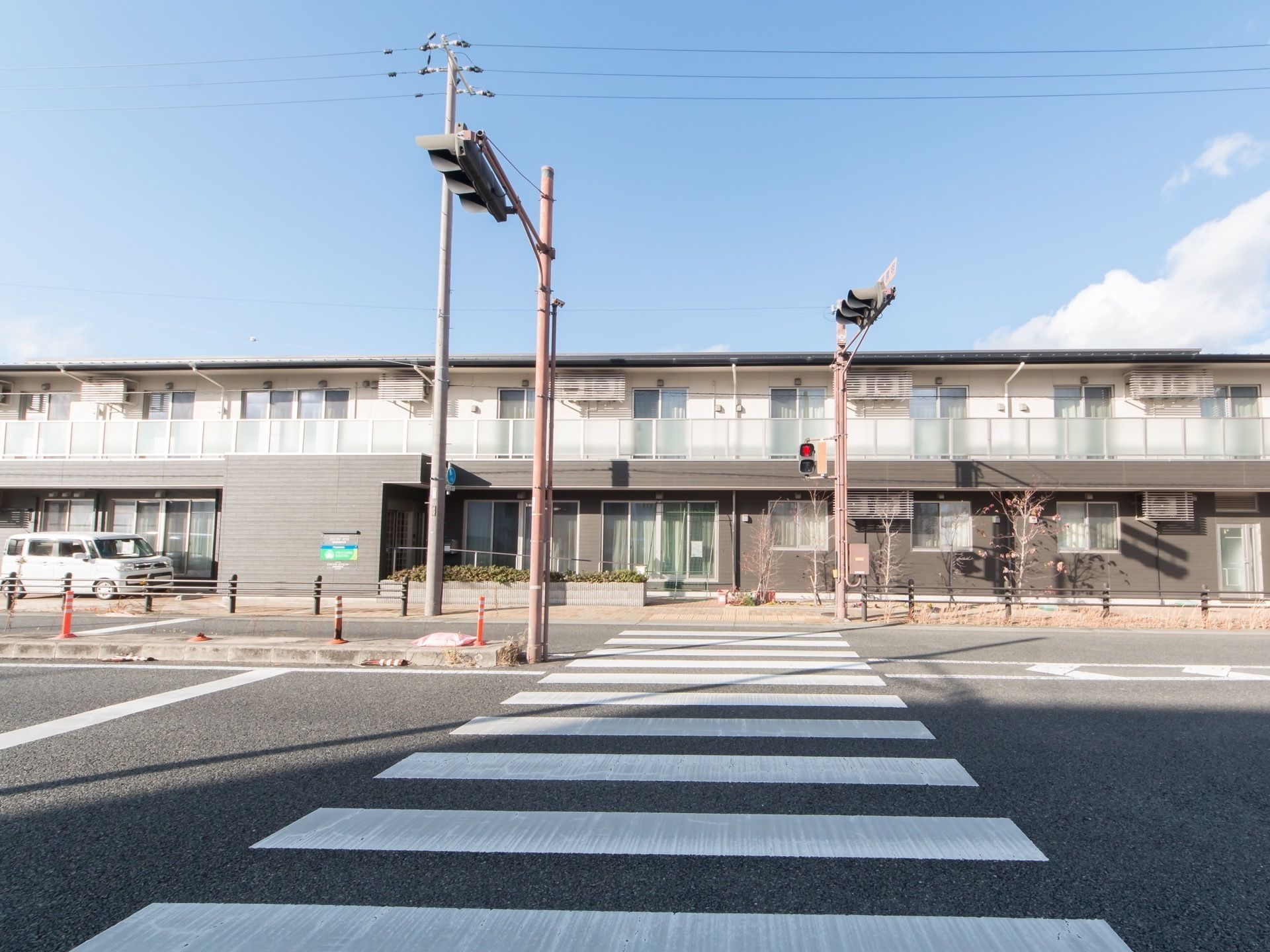 目の前に大きな道路がある敷地に建っている２階建ての施設である。２階には目隠し板がついたバルコニーがある。
