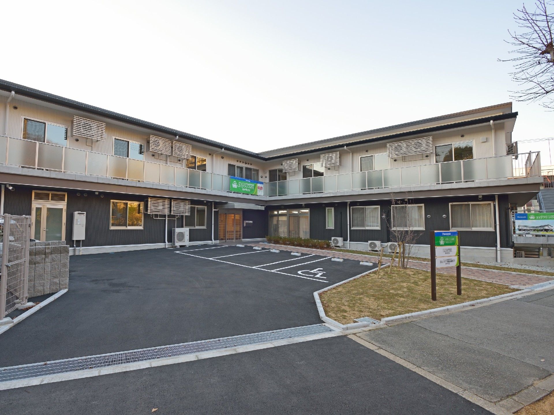 広い駐車場がついた２階建ての建物の前には青、緑などが使われた看板も立っている。