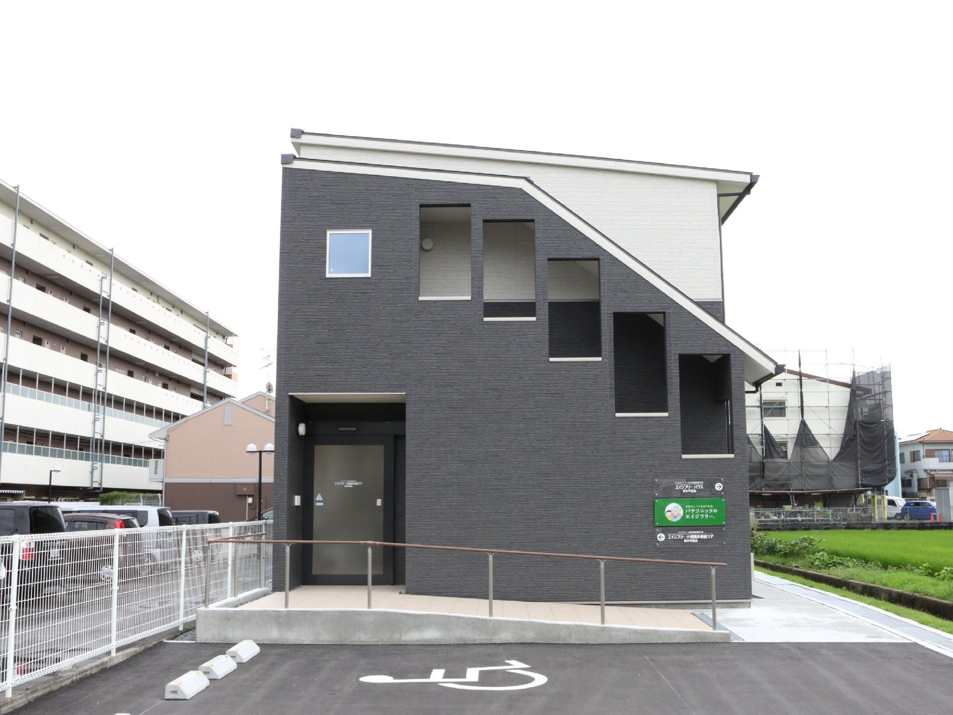 建物の側面から見た様子。玄関には手すり付きのスロープがあり、住宅と併設事業所の名前も書かれている。