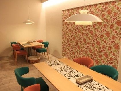 木のぬくもりが感じられるカフェにはカラフルな椅子がセットされた大小のテーブルが置かれ、壁の一部が花柄になっている。