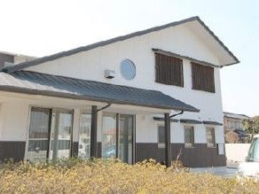 建物は瓦屋根で和の雰囲気。周辺には駐車場や花が植えられたスペースもある。