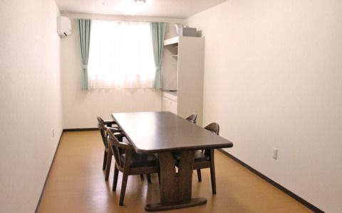 四人掛けのテーブルと椅子がある施設内の談話室の様子