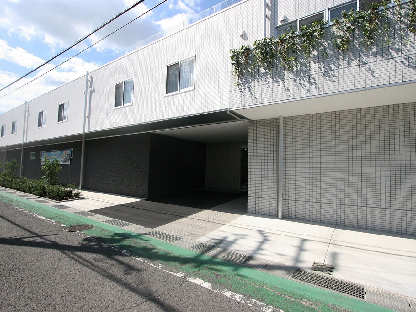 2階建ての建物は横に長く白を基調としていてさわやかな印象。2階部分には窓がたくさんつき、1階の玄関の部分は陰になっていてよく見えない。