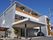 3階建ての建物は現代風のデザインでシルバーと白、ブラウンでまとめられている。玄関には大きな屋根が付き、駐車スペースもあり、各フロアにベランダがある。