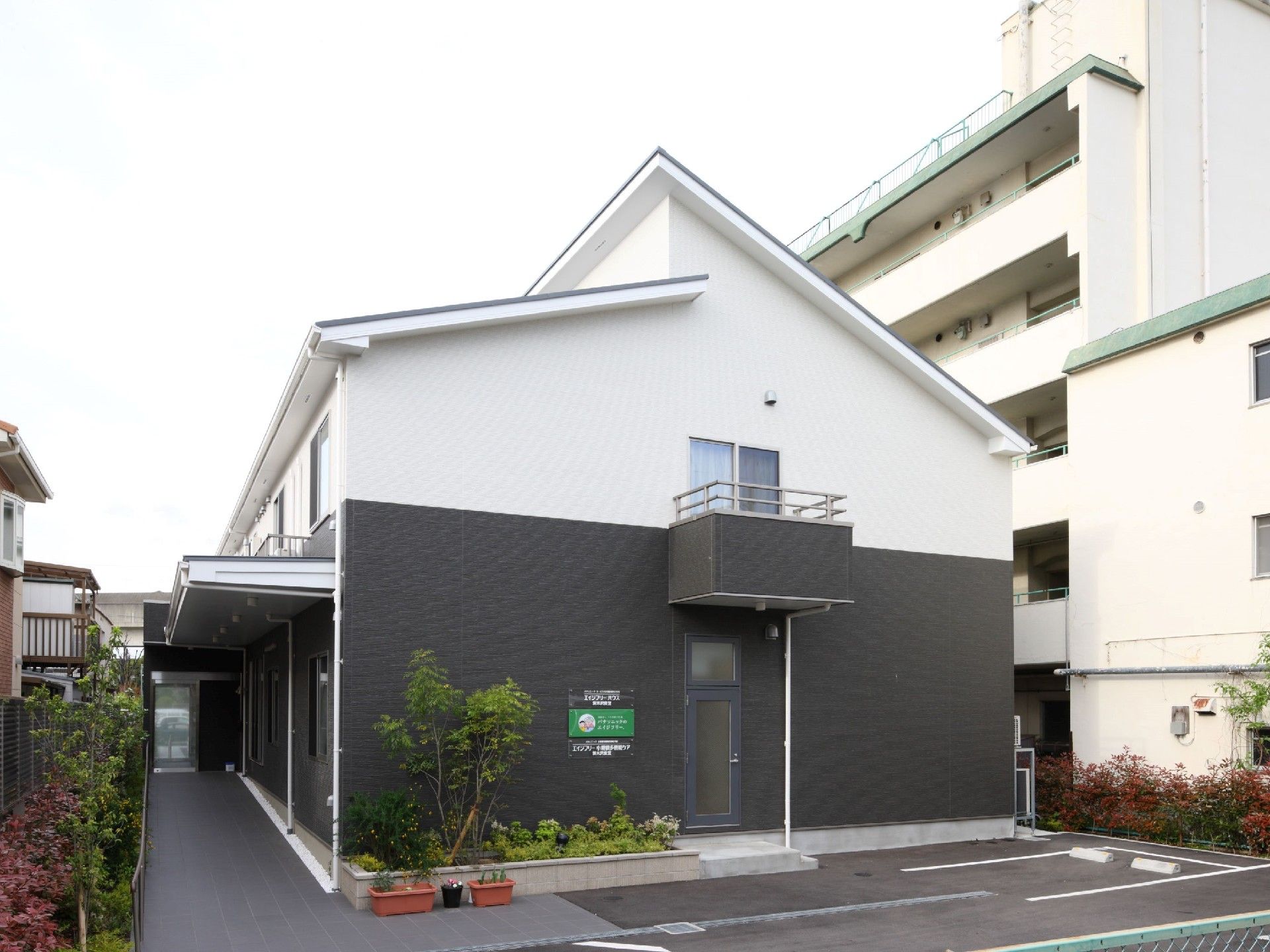 住宅地の中にある２階建ての建物。白とダークグレーで落ち着いた雰囲気。