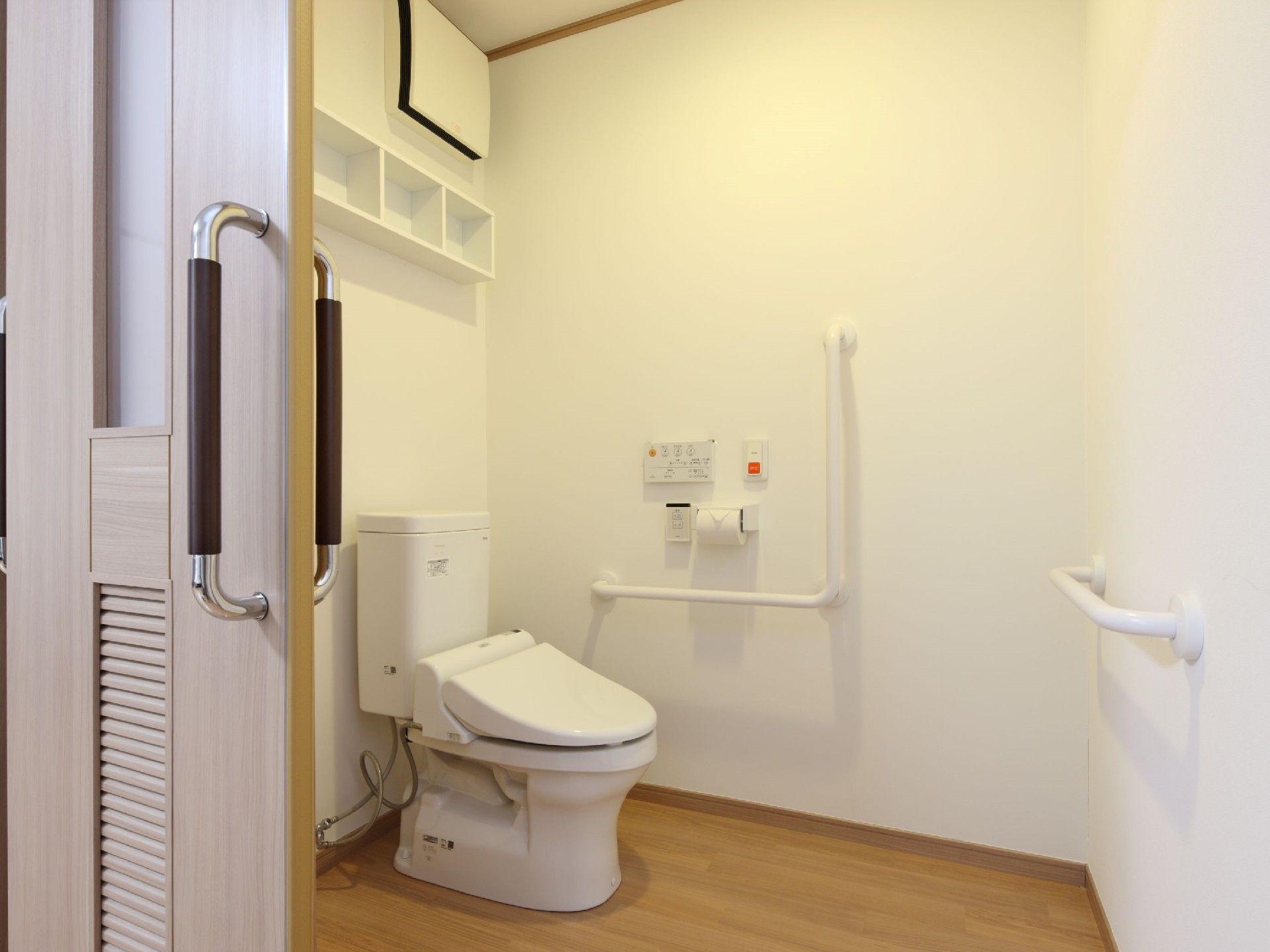 引き戸が付いたトイレは広く、壁にはエル字型の手すりと呼び出しボタン、収納が付いている。