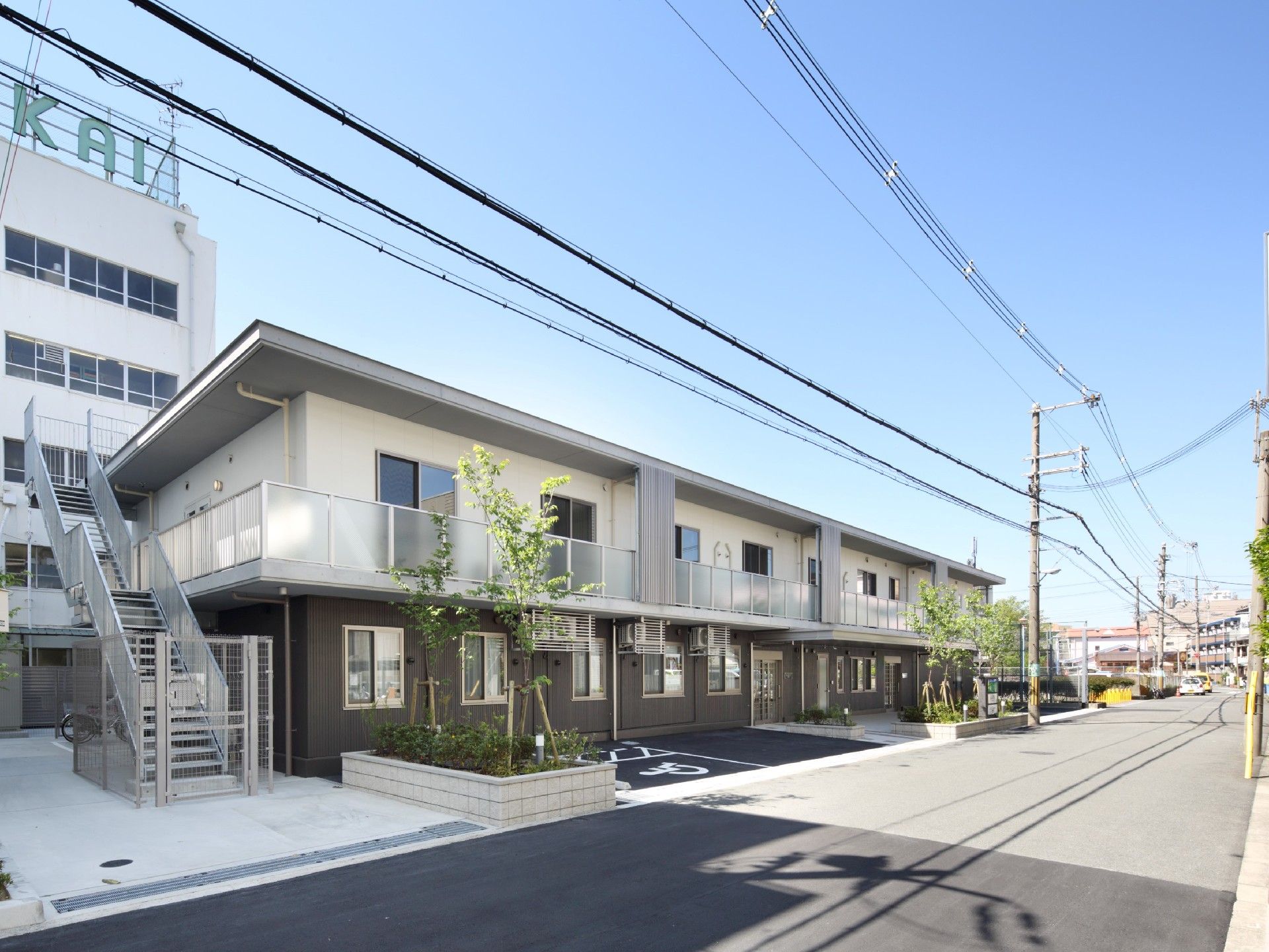 横に長い長方形の建物は2階建てで、1階の一部分がブラウン。駐車スペースもある。