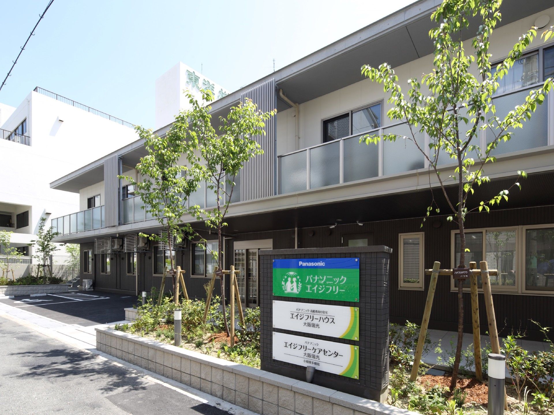 2階建ての建物。1階部分はブラウン、2階部分は白で、玄関の周りには駐車場もある。