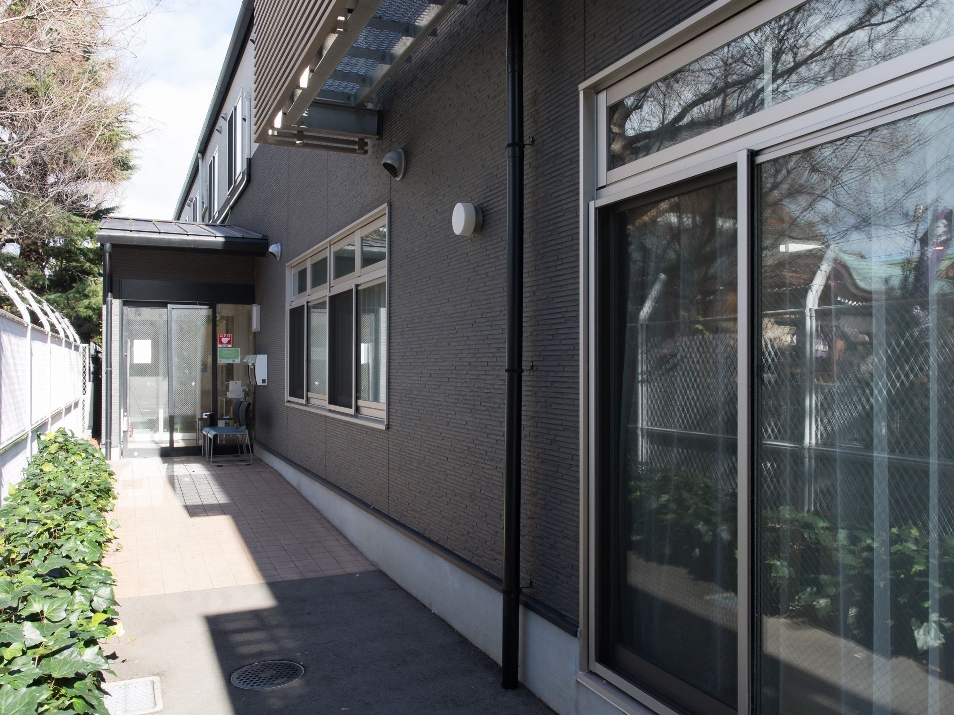 入口へと向かう通路が、建物の側面に沿って設置されている。ドアには、AEDを備えていることを示すシールが貼ってある。
