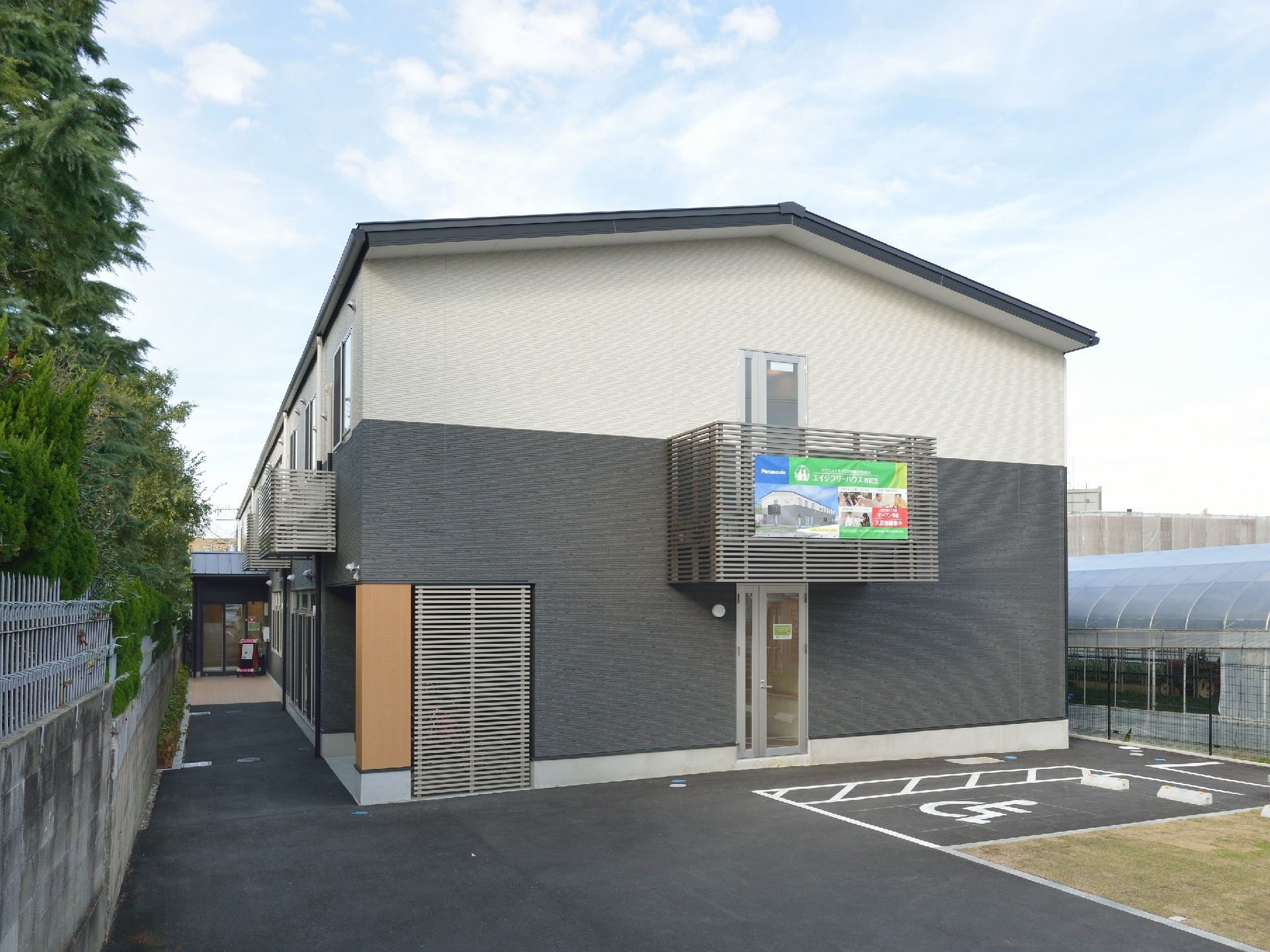 2階建ての建物を側面から見た様子。周辺には緑が多くあり、駐車場もある。