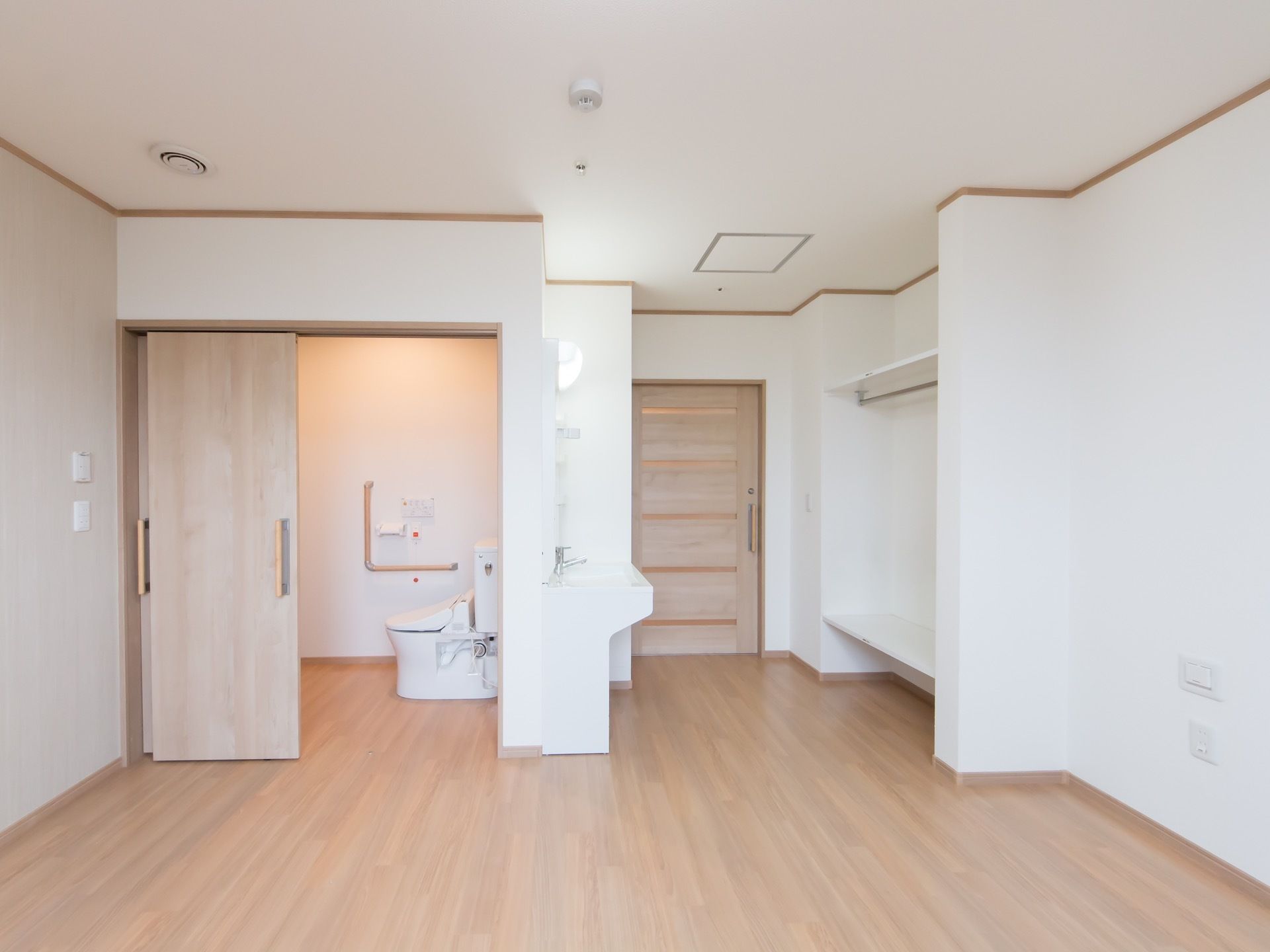 広々とした居室はベージュ色の床と白い壁で明るく温かみのある雰囲気。洗面台、トイレ、オープンクローゼットもある。