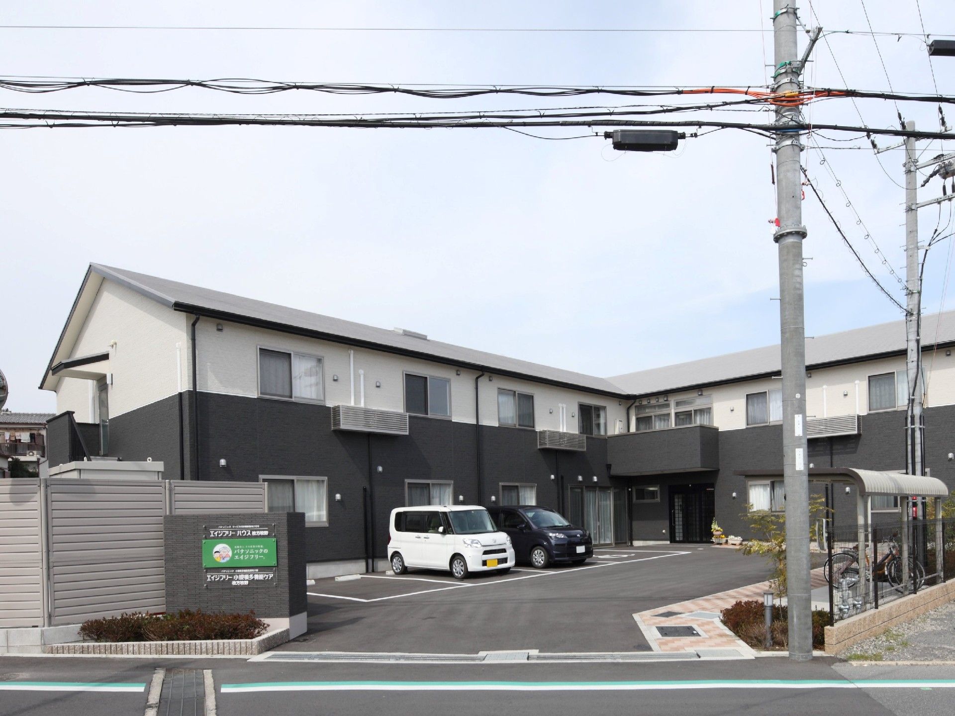 駐車場が付いたベージュの建物。玄関には屋根が付き、駐輪スペースもある。