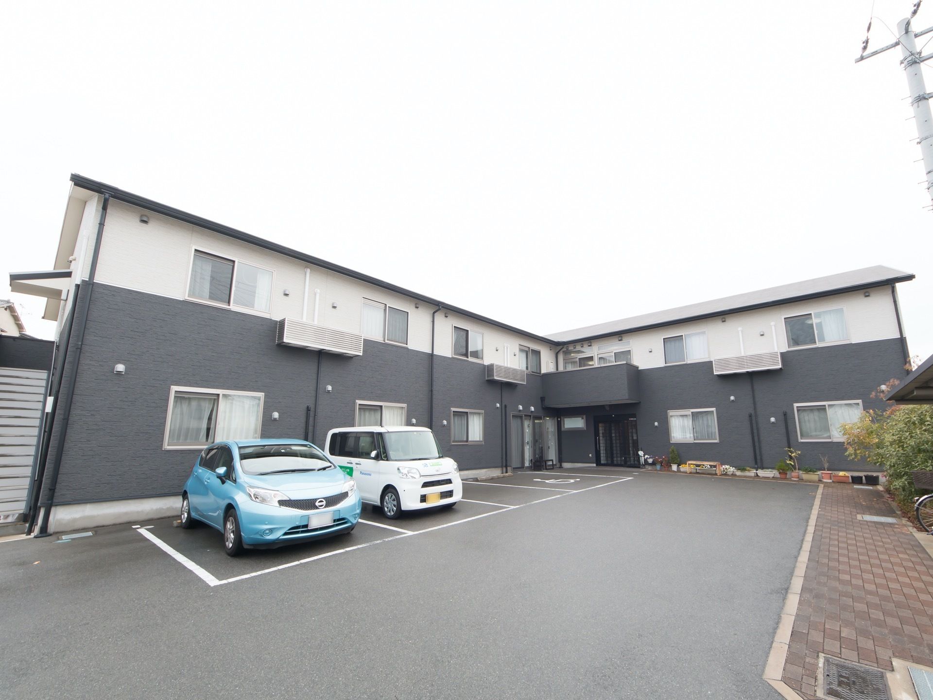 施設は2トーンのモダンな2階建ての建物。施設前の駐車スペースは広く見通しがいい。入口まで平坦で段差がない。