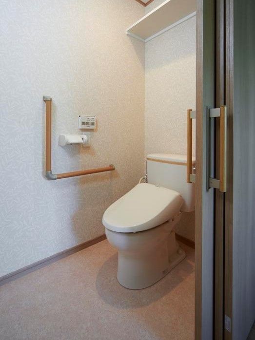 トイレは引き戸でエル字型の手すりや収納棚、操作パネルが付いている。