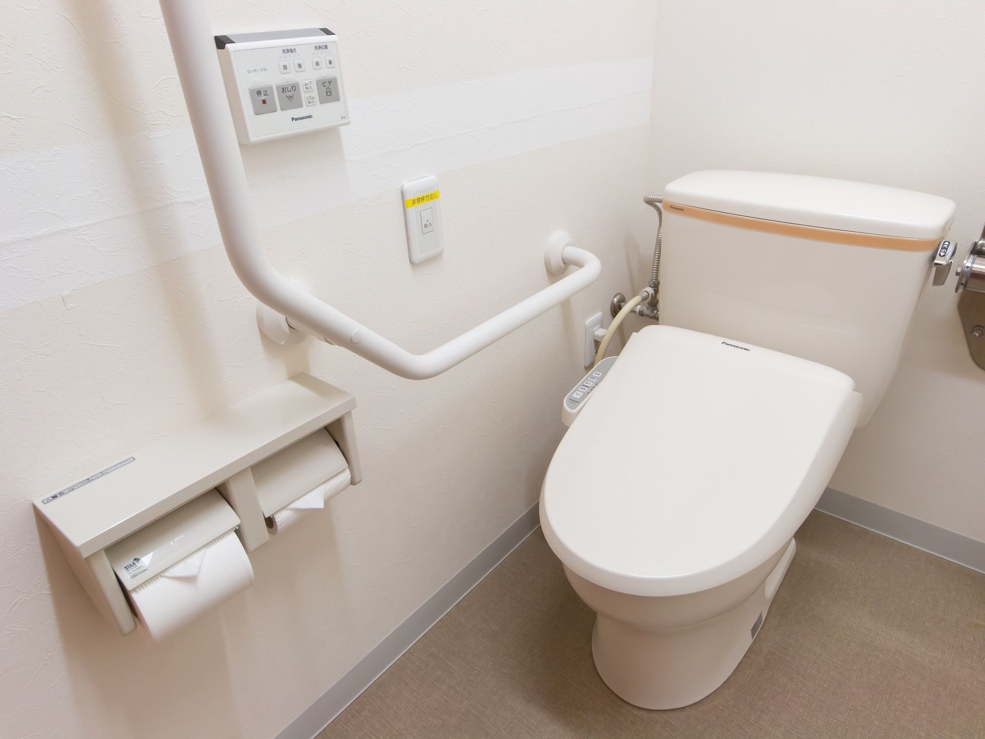 洗浄機能付き便座が設置されたトイレである。横の壁に、手すり、ナースコールが取り付けてある。便器操作盤も横壁にあるので、操作が容易である。