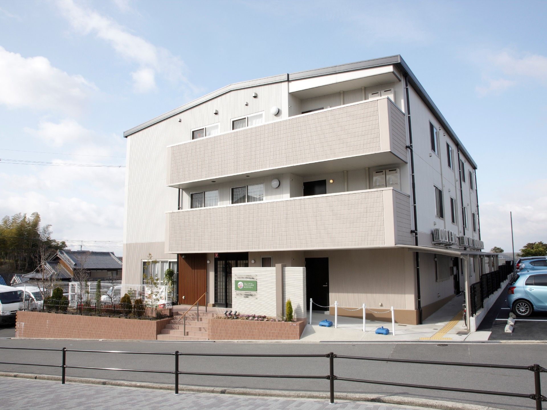 3階建ての建物にはベランダや駐車場がつき、玄関前には階段とスロープがある。